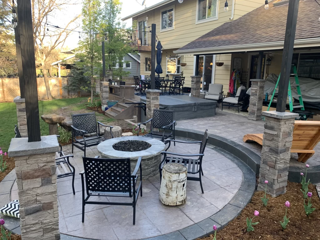 Circular stamped concrete patio with a fire pit seating area and stone pillars in a Denver backyard