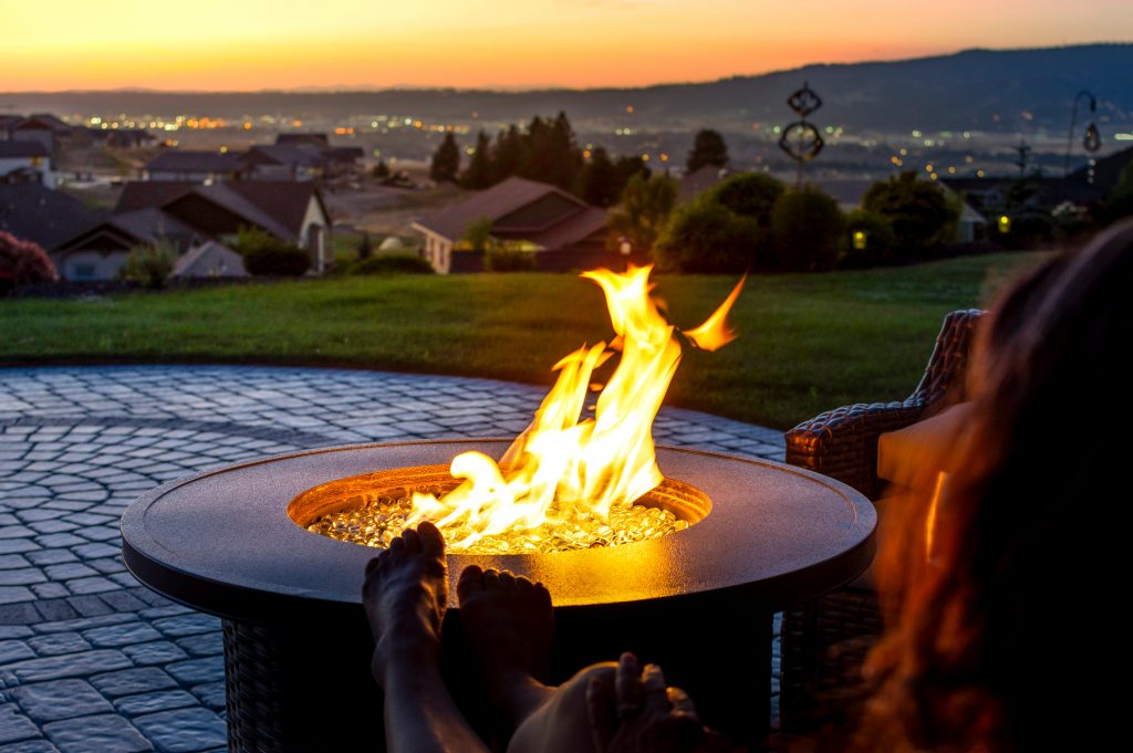 A,Woman,Relaxes,By,A,Roaring,Firepit,On,A,Paver